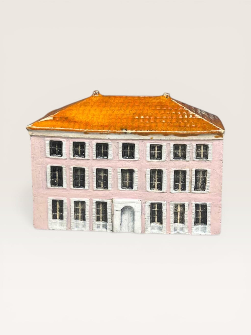 Front view of a handcrafted ceramic miniature house with a pink facade, glazed orange tile roof, and detailed white window frames.