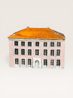 Front view of a handcrafted ceramic miniature house with a pink facade, glazed orange tile roof, and detailed white window frames.
