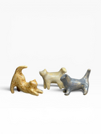 Three small handcrafted ceramic cat figurines in different playful stretching poses (smoky grey, cream, and sandy yellow) on a clean white background