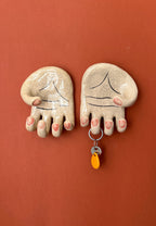 A pair of surrealist ceramic anatomical palm wall hangers (left and right hands) with visible hand-painted life lines mounted against a rich terracotta background.