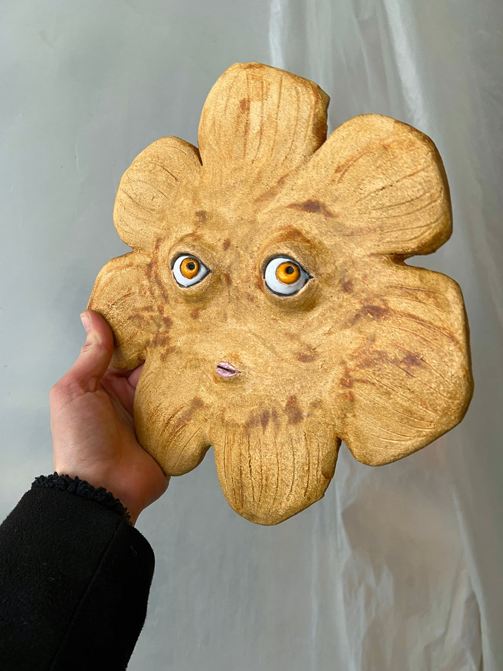 Handmade ceramic sun mask displayed on a gallery wall in a modern bright interior