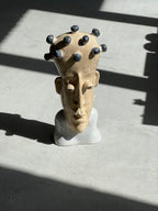 Top-angle view of a handmade ceramic bust sculpture resting on concrete, illuminated by harsh sunlight and shadows.