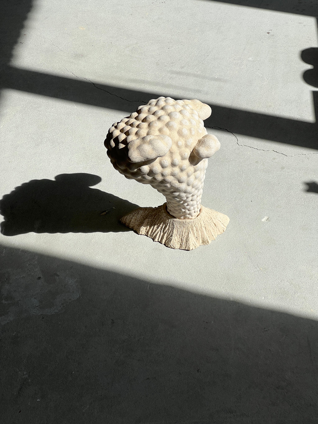 Top view of the beige "Volcano" ceramic sculpture on a concrete surface illuminated by direct sunlight and shadows.